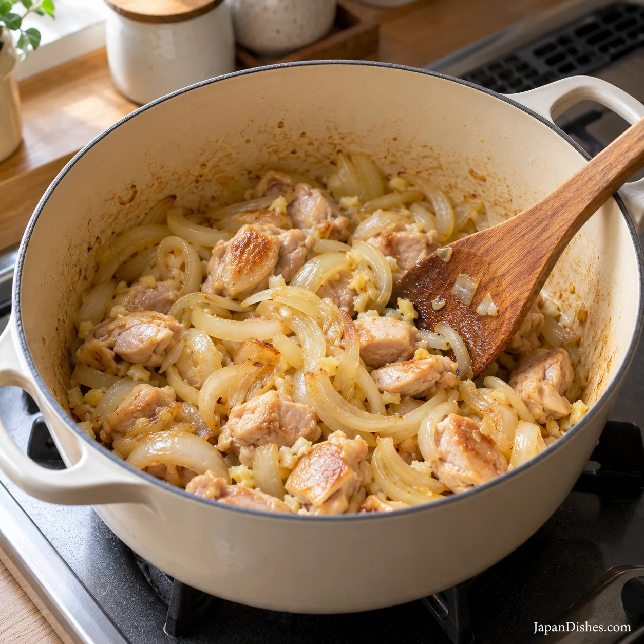 Chicken thigh pieces sautéing with golden sliced onions in an ivory cooking pot