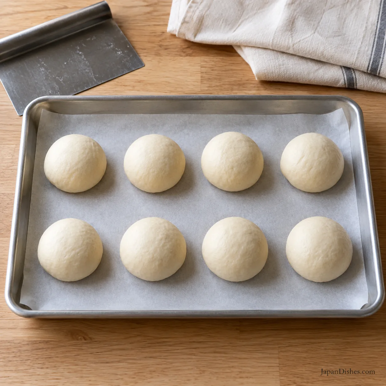 Eight equal smooth dough balls resting on a parchment-lined tray