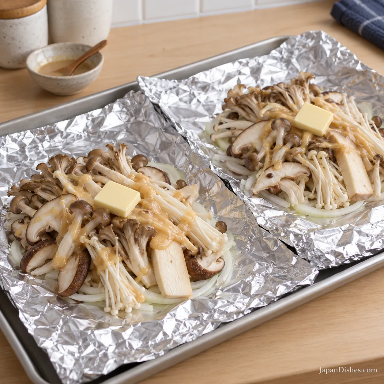 Two open foil sheets with onion, raw mixed mushrooms, miso sauce and one butter piece each