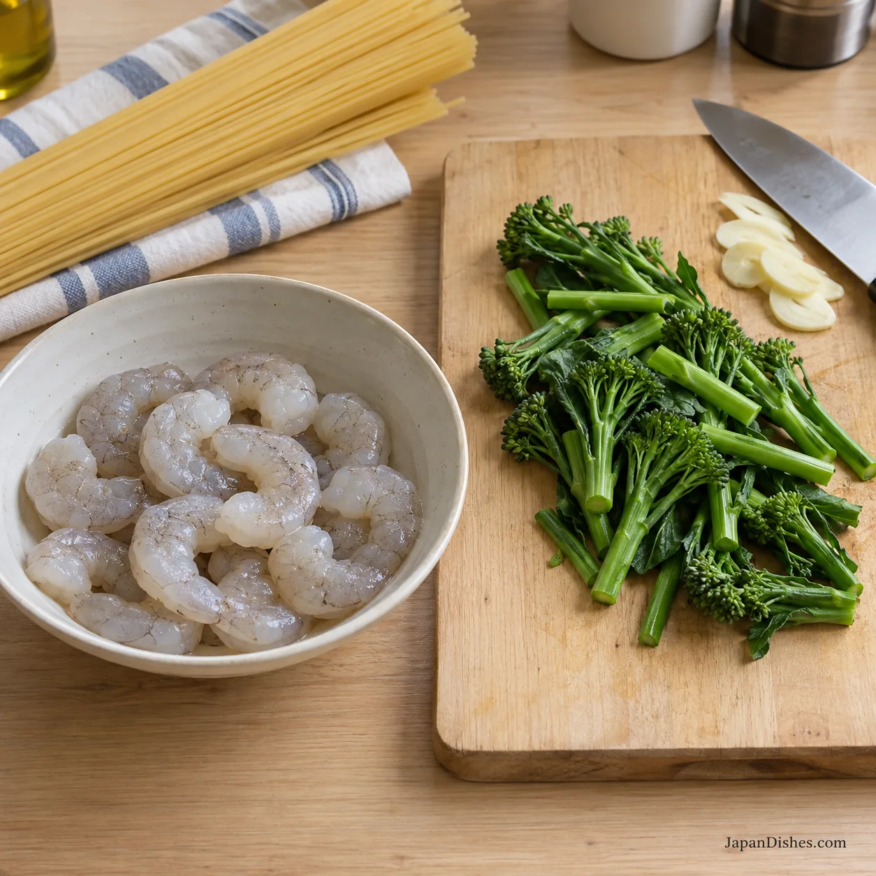 Raw peeled tail-off shrimp in a separate bowl beside cut broccolini and sliced garlic