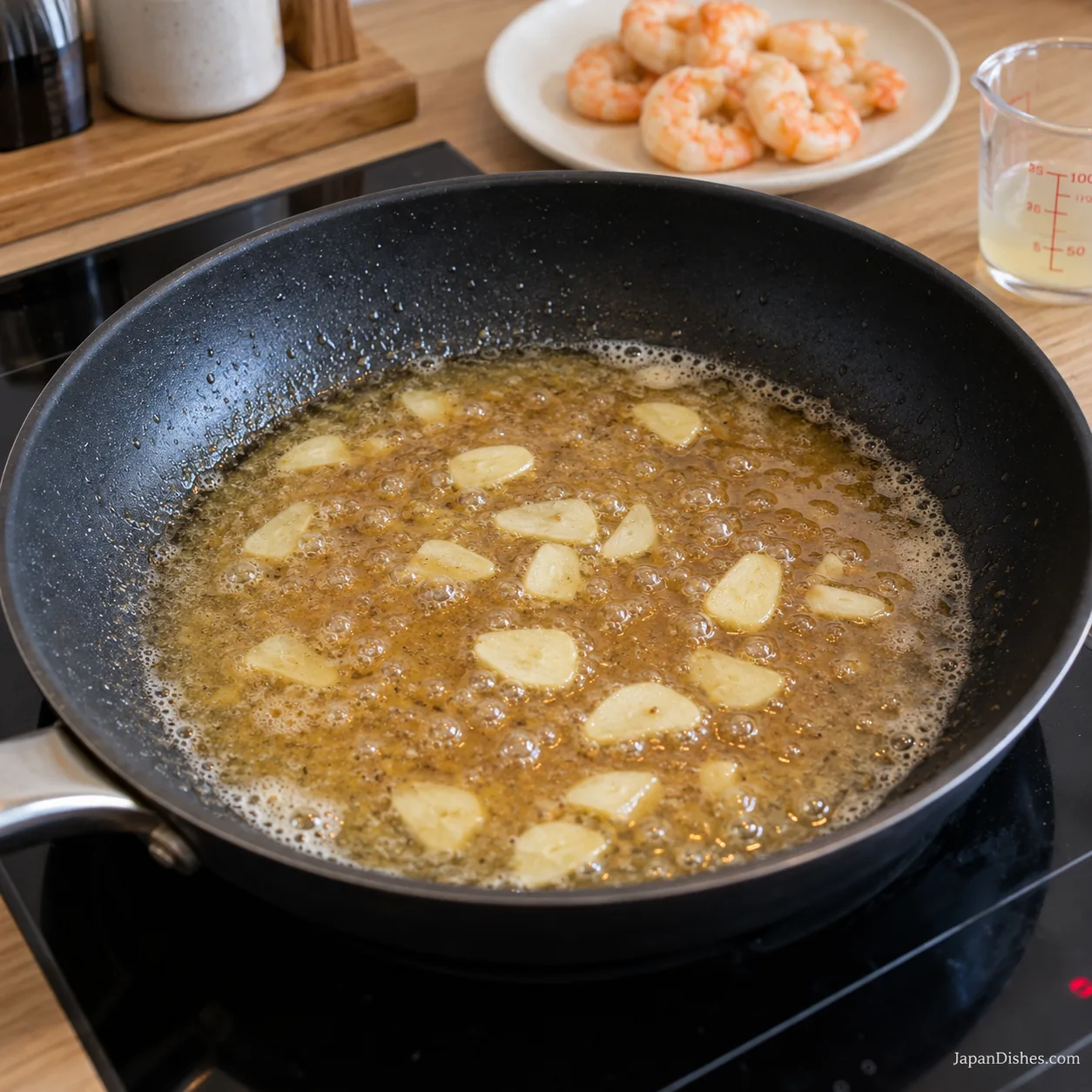Pale sliced garlic in a thin bubbling soy-butter and dashi sauce with cooked shrimp set aside