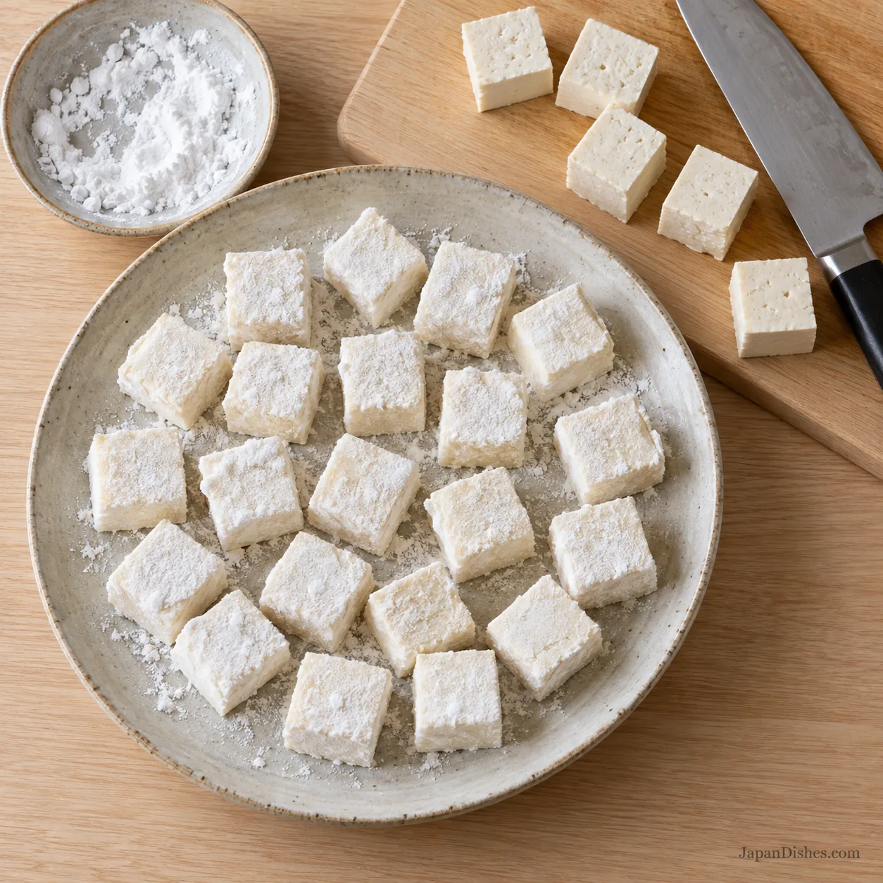 Raw tofu cubes coated with potato starch on an ivory plate before pan-frying