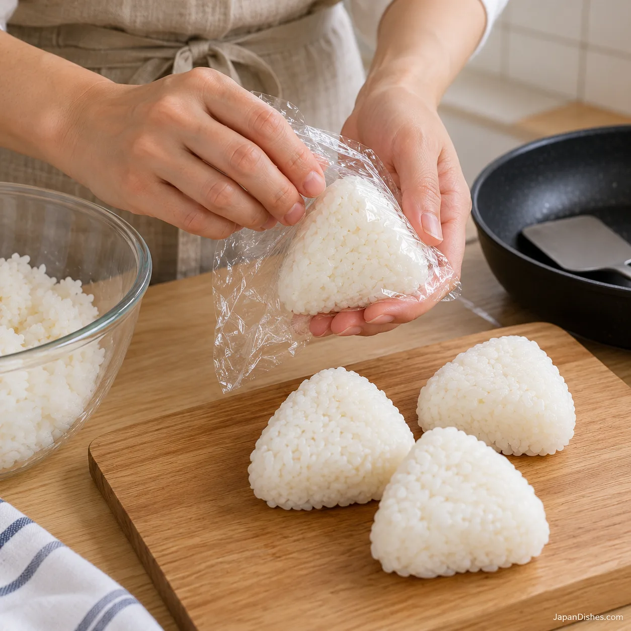 Hands using food-safe plastic wrap to shape a triangular rice ball