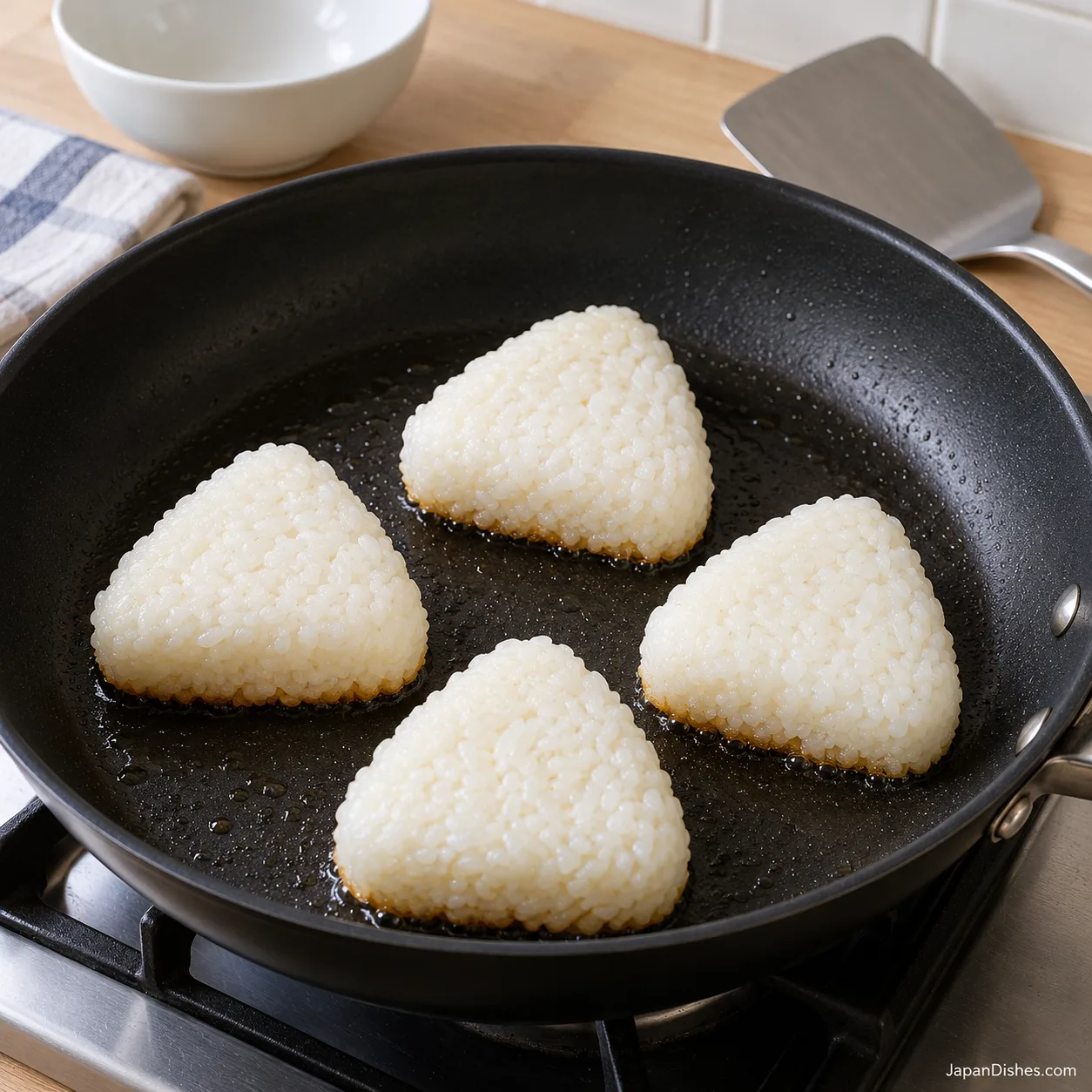 Four rice triangles cooking with white upper faces and golden lower edges