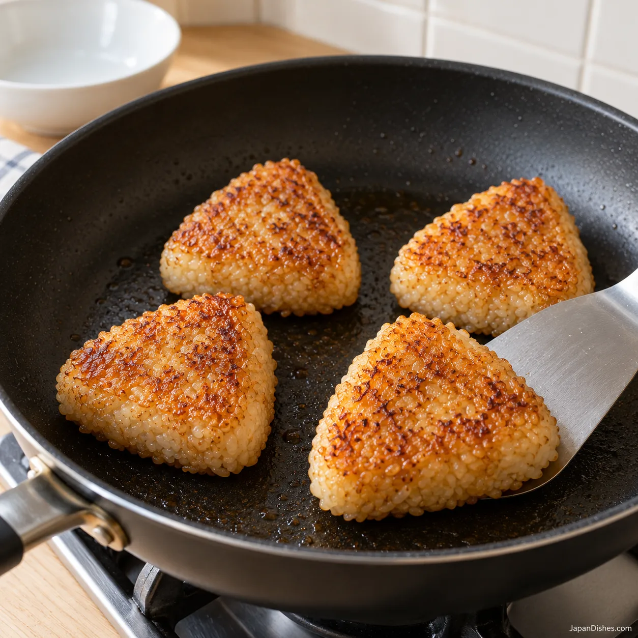 Four yaki onigiri with amber soy-glazed crusts in the pan